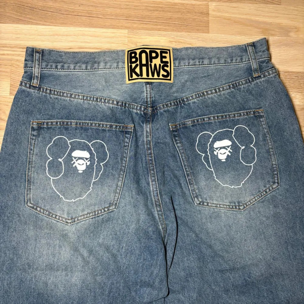 Säljer ett par snygga jeans från A Bathing Ape med det ikoniska Bape Kaws-märket på baksidan. Storleken är L men passar bättre som W32                                            Midjemått tvärs över: 43cm                               Innerbenslängd: 72cm. Jeans & Byxor.