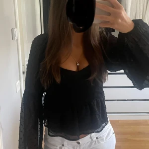 Svart nakd blus - Säljer en snygg svart blus med transparenta, prickiga långa ärmar. Blusen har en  volangdetaljer vid midjan. Perfekt för både vardag och fest! 🖤