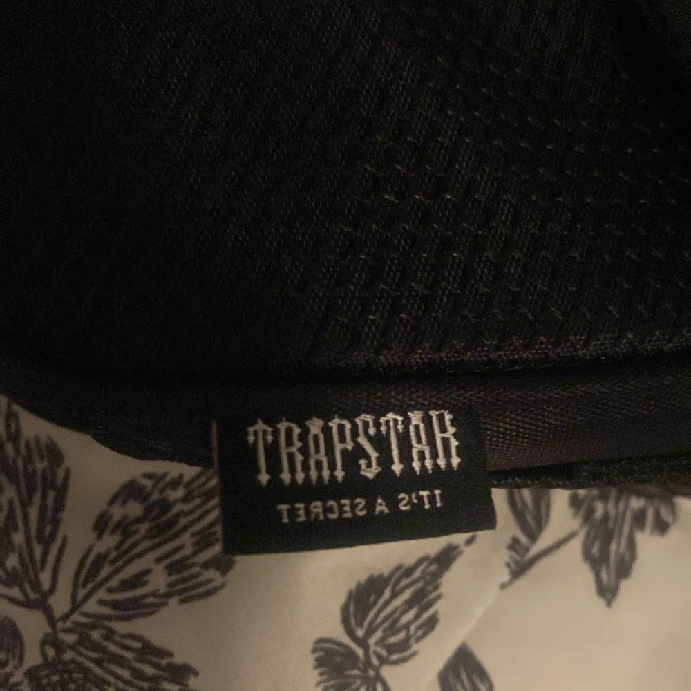 Snygg svart axelväska från Trapstar med en cool spänndetalj på framsidan. Väskan är perfekt för vardagsbruk och har en justerbar axelrem. Den är gjord i ett slitstarkt material och har en unik design som verkligen sticker ut. Perfekt för att ge din outfit en edgy touch!. Väskor.