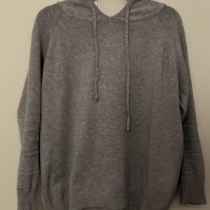 Merinoull hoodie - Mysig grå hoodie i 100% merinoull. Perfekt för kyliga dagar med sin bekväma passform och praktiska huva. Den har långa ärmar och ribbade muddar för extra komfort. Perfekt för både vardag och avslappnade stunder.