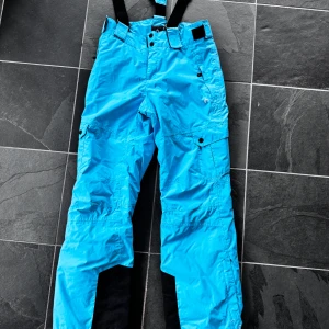 Blå skidbyxor med hängslen - Blå skidbyxor. De har justerbara svarta hängslen och flera praktiska fickor med knappar. Perfekta för vinterns äventyr i backen! ❄️  Rensar ur min garderob just nu🌼 Kika och se om du ser något mer i min profil som du gillar så skickar jag med det till dig också!😊 Fler kläder kommer! 