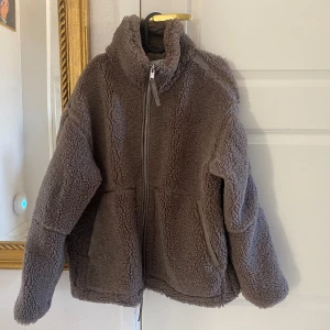 Ny mörkbeige teddyjacka pilejacka från HM - Ny med tags. En mörkbeige brun tjock och varm teddyjacka i mjuk pile med kantband i ytbehandlad kvalitet. Jackan har lös passform, ståkrage, tvåvägsdragkedja fram och kängurufickor. Fodrad. Storlek: M (oversize)