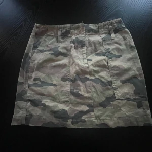 Camouflage kortkjol - Säljer en supercool camouflage kortkjol i bomull. Perfekt för en avslappnad och trendig look. Kjolen har praktiska fickor både fram och bak, och en bekväm passform. 