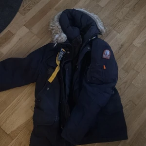 Mörkblå parkajacka med pälsdetaljer large herr storlek - Säljer en mörkblå parkajacka från Parajumpers i mycket bra skick. Jackan har en mysig pälsfodrad huva och quiltad insida för extra värme. Perfekt för kalla vinterdagar! Den har praktiska fickor och en snygg gul detalj vid halsen. Passar både till vardags och äventyr.