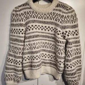 Vit och brun stickad tröja - Mysig stickad tröja i vitt och brunt med ett snyggt mönster. Perfekt för kalla dagar med sin varma och sköna känsla. Tröjan har långa ärmar och ribbade muddar vid ärmslut och nederkant. Passar perfekt till höst- och vintergarderoben! Storlek M - fint skick!