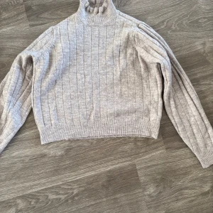 Beige stickad polotröja - Mysig beige stickad polotröja med ribbade detaljer. Perfekt för kyliga dagar med sin varma och bekväma passform. Tröjan har långa ärmar och en hög krage som håller dig varm. Passar både till vardags och lite finare tillfällen. 🧶✨