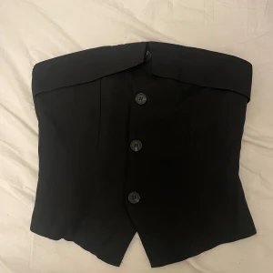 Svart korsettliknande topp - Snygg svart korsettliknande topp med knappar framtill. Perfekt för en festlig kväll eller en stilren look. Har bara provat toppen en gång men sen har den aldrig kommit till användning. Skulle säga att den är normal i storleken. 