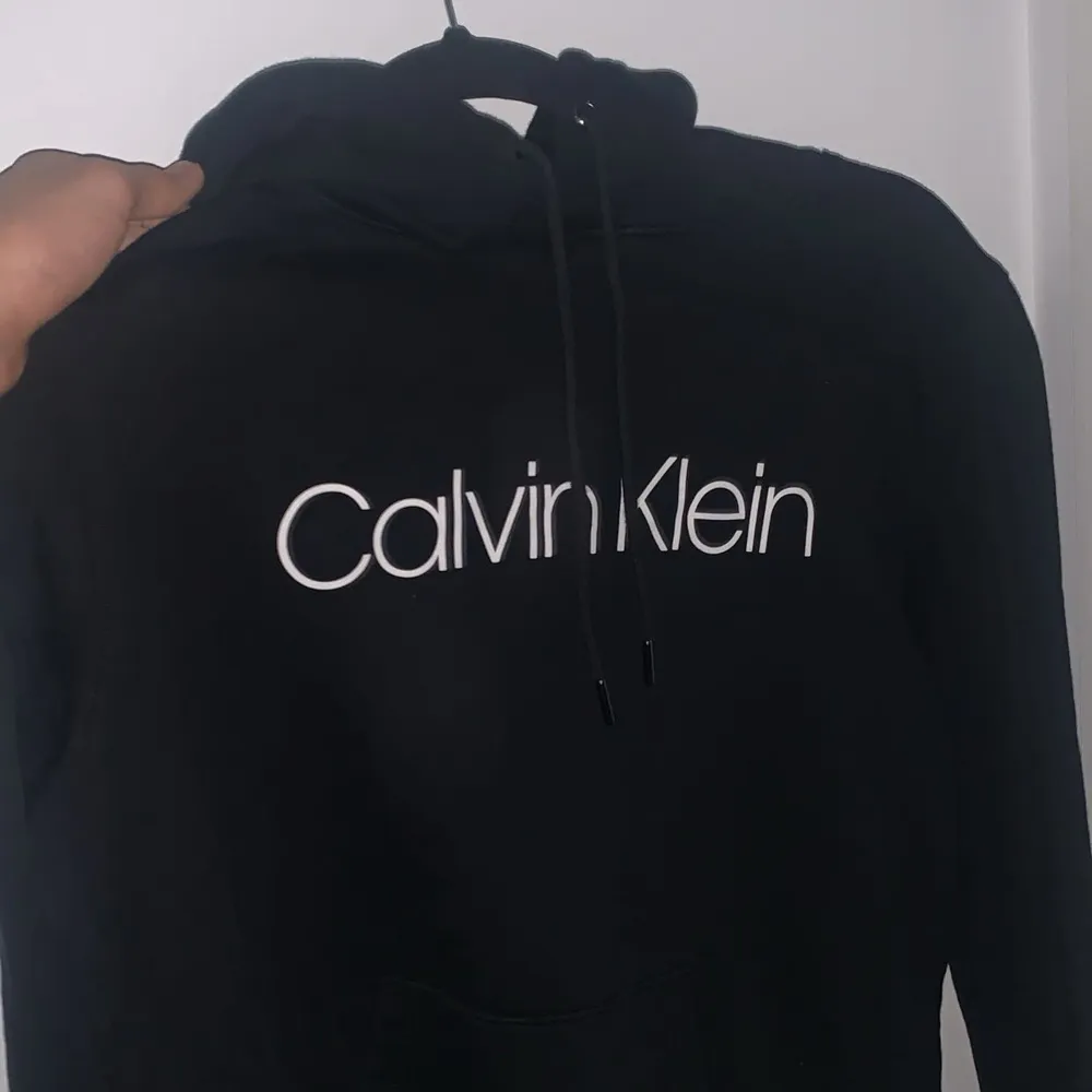 Säljer en stilren svart hoodie från Calvin Klein. Den har en klassisk passform med justerbar huva och det ikoniska Calvin Klein-logotypen tryckt på framsidan. Perfekt för en avslappnad look eller att mysa i hemma. Passar till alla säsonger!. Neuletakit & Villapaidat.