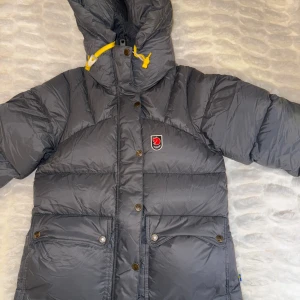 Grå dunjacka från Fjällräven women xs - Intressekol på min grå dunjacka från Fjällräven i mycket bra skick. Nypris: 7000❄️Jackan har en varm och vadderad design med huva. Perfekt för kalla vinterdagar. Den har både dragkedja och knappar framtill. 