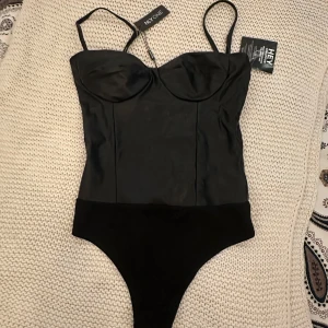Svart skinn body - Helt ny svart f”ke läder body från Nelly, den har justerbara axelband och är väldigt stretchig