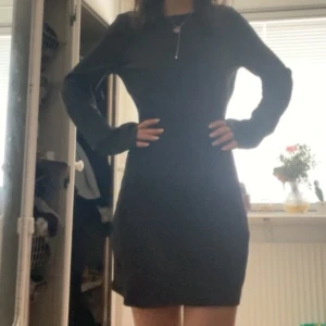 Svart klänning med öppen rygg - Snygg svart satin klänning i mycket bra skick med en stilren design. Den har en öppen rygg och långa ärmar, perfekt för både fest och vardag. Klänningen är tight och kort, vilket ger en elegant och modern look. Passar perfekt för höst och vinter.