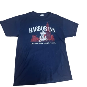 Mörkblå t-shirt grafik - Säljer en mörkblå t-shirt med tryck av 'Harbor Inn' i Cleveland, Ohio.  Den är i bra skick och passar perfekt till vardags. Passar som en medium.