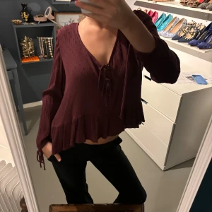 Vinröd blus med volangdetaljer - Säljer en superfin vinröd blus med volangdetaljer och knytning framtill. .