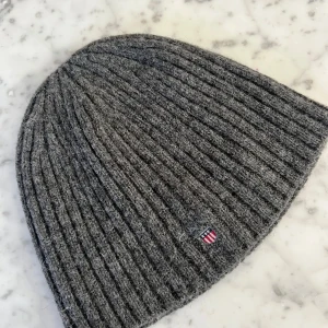 Grå ribbad mössa från GANT - Säljer en snygg grå ribbad mössa från GANT i ull. Den är i one size och har en liten broderad logga på sidan. Perfekt för att hålla sig varm under höst och vinter. Mössan är i mycket bra skick och redo för nya äventyr!