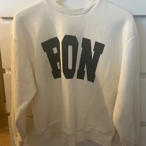 Vit sweatshirt med tryck - Säljer en vit sweatshirt med stort svart tryck 'BON' på framsidan. Tröjan är i bra skick och har en klassisk rund halsringning. Perfekt för en avslappnad stil och passar till både jeans och joggers. Skön och enkel att matcha! 🖤