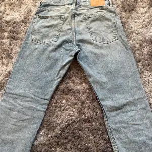 Säljer ett par klassiska blå jeans från Jack & Jones i bra skick. De har en normal passform och är tillverkade av bomull. Perfekta för vardagsbruk med en tidlös stil. Dragkedja och knapp framtill, samt fem fickor. Passar både vår och höst.