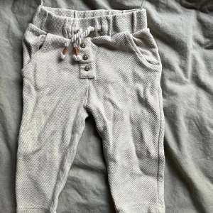 Beige babybyxor från C&A - Säljer ett par supermjuka och bekväma beige babybyxor från C&A. De har en elastisk midja med snörning och knappar framtill för extra stil. Perfekta för både lek och mysiga stunder. Passar barn i åldern 9-12 månader.