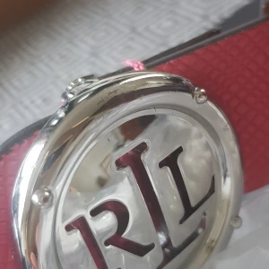 Brunt och rött bälte från Ralph Lauren - Säljer ett snyggt bälte från Ralph Lauren i brunt och rött. Bältet har en cool RL-logga i silver på spännet och är gjort av skinn. Perfekt för att ge din outfit en extra touch! 👜