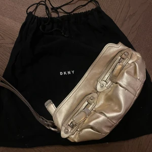Guld axelväska från DKNY - Snygg guld axelväska från DKNY med stilrena detaljer. Perfekt för att ge din outfit en lyxig touch. 