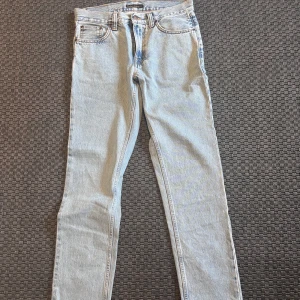 GRITTY JACKSON - Nudie Jeans - Snygga ljusblå jeans från Nudie Jeans med klassisk femficksdesign och knappgylf. Perfekta för en avslappnad stil. De har en broderad detalj på bakfickan och är tillverkade i slitstarkt denim.   STRL W30 L32