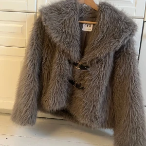 Grå pälsjacka från Zara - Säljer en snygg grå pälsjacka från Zara med stora hakar framtill. Jackan har en fluffig och lyxig känsla. Jackan är i nyskick. 