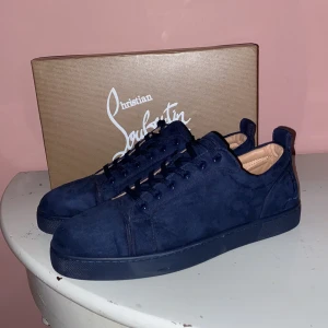 Loubs - Snygga mörkblå sneakers i mocka från Christian Louboutin med den ikoniska röda sulan. Skorna har en stilren design med snörning och en bekväm passform. Perfekta för att ge din outfit en lyxig touch. Tveka inte för minsta fråga!