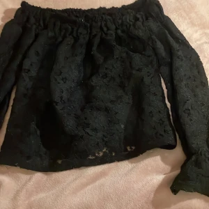 Svart spetsblus  - Säljer en elegant svart spetsblus med offshoulder-design. Blusen har långa ärmar och ett vackert spetsmönster som ger en romantisk känsla. Perfekt för att lyfta vilken outfit som helst.