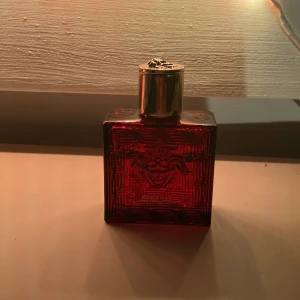 Versace Eros Flame Eau de Parfum - Säljer en elegant Versace Eros Flame Eau de Parfum i en fyrkantig röd flaska med ett detaljerat mönster och ett gyllene lock. Perfekt för den som vill ha en doft med intensitet och stil.