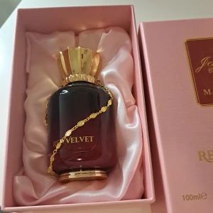 Red Velvet, EDP,  Maison Asrar - Upptäck den lyxiga Red Velvet parfymen från Maison Asrar. Flaskan har en elegant design med en gradient av rött och svart, dekorerad med en gyllene kedja och lock. Förpackningen är i en stilren rosa ask med gyllene detaljer. Perfekt för den som söker en sofistikerad doftupplevelse.