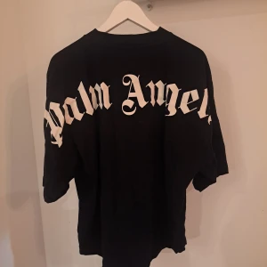 Svart t-shirt från Palm Angels - Snygg svart t-shirt från Palm Angels med stort tryck på ryggen och mindre tryck där fram. Tillverkad i mjuk bomull för en bekväm känsla. Perfekt för en avslappnad stil.