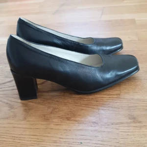 Svarta pumps från Ecco - Eleganta svarta pumps från Ecco i skinn med en bekväm klack. Skorna har en klassisk design med fyrkantig tå och en stilren look. Perfekta för en chic och tidlös stil.