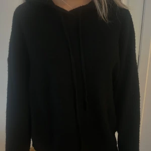 Svart hoodie - Säljer en stilren svart stickad hoodie med långa ärmar och dragsko i halsen. Perfekt för en avslappnad look.