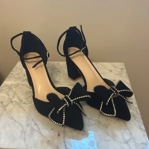 Svarta pumps med rosett och klack - Söta svarta pumps med spetsig tå och dekorativ rosett prydd med pärlor. bekväm klack storlek 38 oanvända 