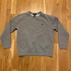 Grå sweatshirt från Polo Ralph Lauren - Säljer en grå tröja från Polo Ralph Lauren. Tröjan har en rund halsringning och ett diskret broderat märke på bröstet. Knappt använd  