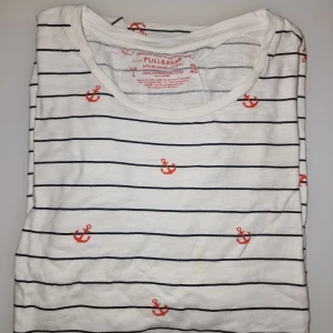 Randig t-shirt med ankare från Pull&Bear - Perfekt för en avslappnad stil med en maritim touch. T-shirten är kortärmad och gjord i bomull för en skön känsla. Garderobsrensning så kika gärna på övriga auktioner.