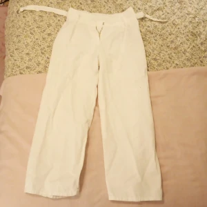 Vita byxor med bälte - Säljer ett par vita byxor med tillhörande bälte. Byxorna har en rak passform och är högmidjade. Perfekta för en stilren look.140 barnstorlek.