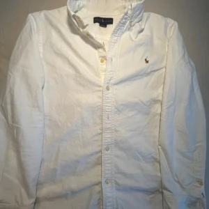 Vit Ralph Lauren skjorta  - Säljer en klassisk vit skjorta från Ralph Lauren. Skjortan är lång ärmad och knappar längst med skjortan. Skicket på skjortan är 8/10.             Skjortan är Äkta och original 