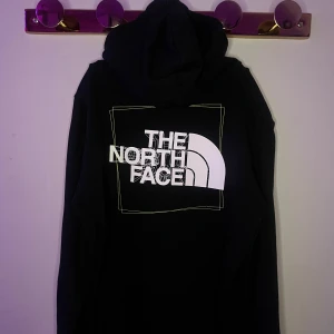 Svart hoodie från The North Face - Säljer en svart hoodie från The North Face med logga både fram och bak. Hoodien har en klassisk design med dragsko i huvan och en stor ficka framtill. Perfekt för en avslappnad stil.