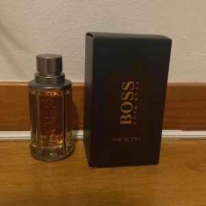 Hugo Boss The Scent Parfym - Säljer en elegant parfym från Hugo Boss, The Scent. Flaskan är stilren med en metallisk kork och genomskinligt glas som visar den gyllene vätskan. Förpackningen är svart med guldtext. Perfekt för den som vill ha en sofistikerad doft. Använd 3-5 gånger so. Ny skick.