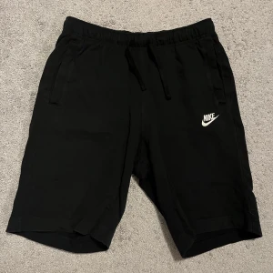 Svarta shorts från Nike - Snygga svarta shorts från Nike med elastisk midja och snörning. Perfekta för träning eller en avslappnad dag. Nike-loggan i vitt på benet ger en sportig touch.