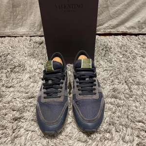 Valentino Garavani sneakers i blått och grått - Snygga Valentino Garavani sneakers i en kombination av blått och grått. Skorna har en stilren design med mörkblåa snören och detaljer i mocka och skin. Skick 8/10 + dust bag och box. Hör av er vid frågor eller fundering! Pris kan diskuteras!