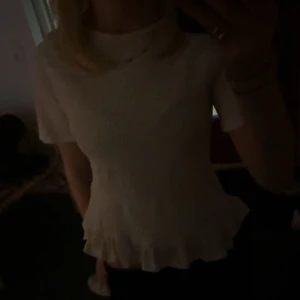 Vit topp med volangdetalj - Säljer en söt vit topp med korta ärmar och volangdetalj vid nederkanten. Från Gina tricot och helt ny🤍