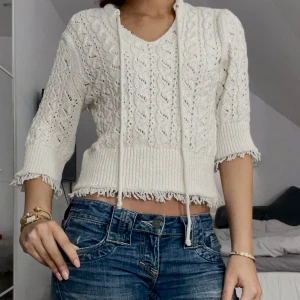 Vit stickad tröja med knyt - Säljer en söt vit stickad tröja med knyt i halsen och trekvartsärmar. Tröjan har ett fint spetsmönster och ribbade kanter. Perfekt för en avslappnad stil. Passar bra till jeans eller kjol.