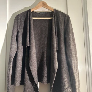 Brun kofta från frk - Säljer en stilren brun kofta från frk. Den har en öppen design med långa ärmar och ett mjukt, stickat material som passar perfekt för kyligare dagar. Perfekt att slänga över en topp för en avslappnad look.