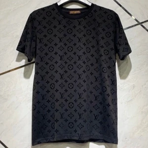 Svart t-shirt från Louis Vuitton - Snygg svart t-shirt från Louis Vuitton med ett diskret mönster av märkets ikoniska logotyper. Tillverkad i 100% bomull för en bekväm passform. Perfekt för dig som vill ha en stilren look med en touch av lyx.
