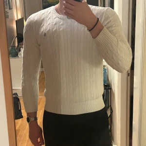 Vit stickad tröja från Ralph Lauren - Säljer en stilren vit stickad tröja från Ralph Lauren med kabelstickat mönster. Tröjan har långa ärmar och en rund halsringning. Modellen är 190cm, storlek XL