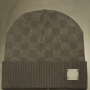 Grå mössa från Louis Vuitton - Snygg grå mössa från Louis Vuitton med diskret rutmönster och ribbad kant. Märkesplatta framtill ger en exklusiv touch. Perfekt för kyliga dagar.