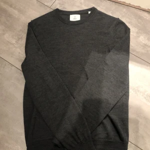 Mörkgrå tröja från Bläck - Säljer en stilren mörkgrå tröja från Bläck. Tröjan har en klassisk design med långa ärmar och rund halsringning. Perfekt för en enkel och snygg look.
