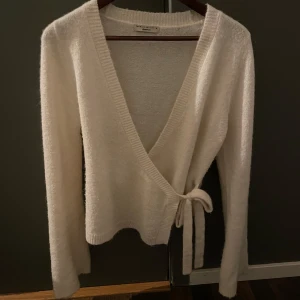 Vit omlottkofta från Gina tricot - Säljer en vit omlottkofta från Gina tricot. Koftan har en v-ringad design med knytband i sidan och långa ärmar. Den är i nyskick då den bara är använd ca 2 gånger💓