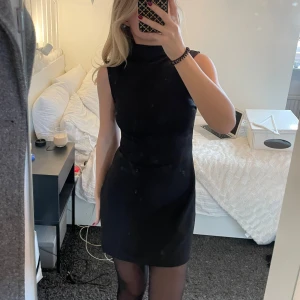 Svart elagant klänning - Snygg svart ärmlös klänning med hög sne krage. Elegant och ger en tight passform. Helt ny utan prislappar